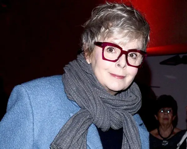 Karolina Korwin Piotrowska w okularach i niebieskim płaszczu, z szarym szalem na szyi.