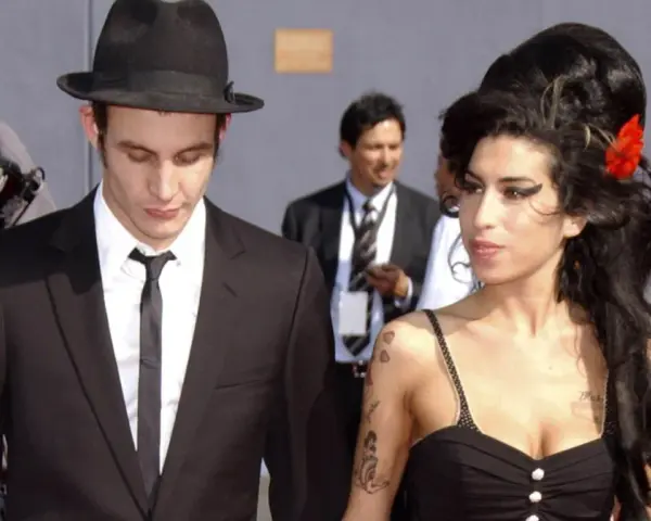 Blake Fielder-Civil w czarnym garniturze i kapeluszu obok Amy Winehouse z czerwoną różą we włosach.