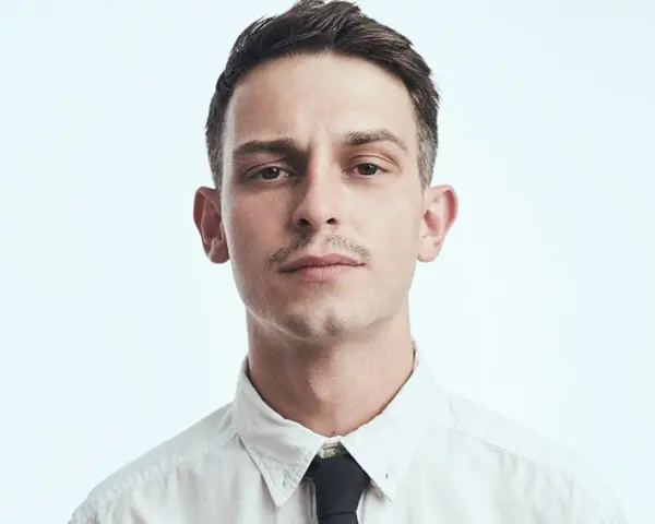 Młody mężczyzna, Vito Bambino, w białej koszuli i czarnym krawacie. Jego wzrost jest imponujący, a spojrzenie intensywne.