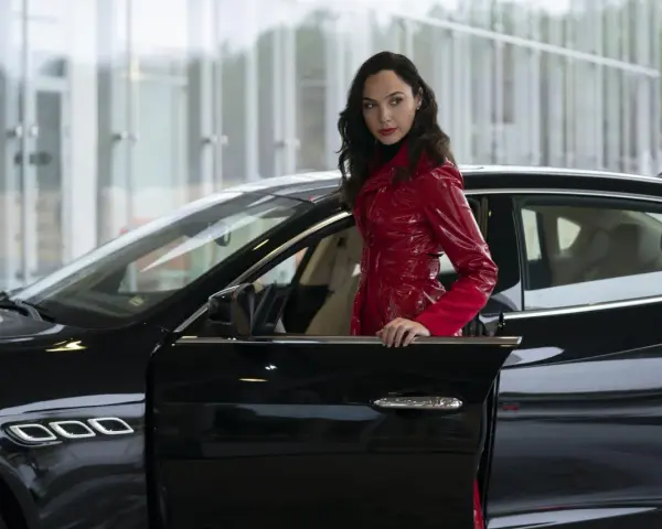 Kobieta w błyszczącym, czerwonym płaszczu opiera się o czarne auto. Wygląda jak z filmu, może to jej czerwona nota 2?
