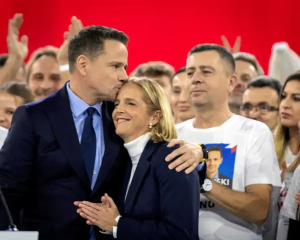 Rafał Trzaskowski, choć nie znamy jego dokładnego wieku, czule całuje żonę na tle tłumu.