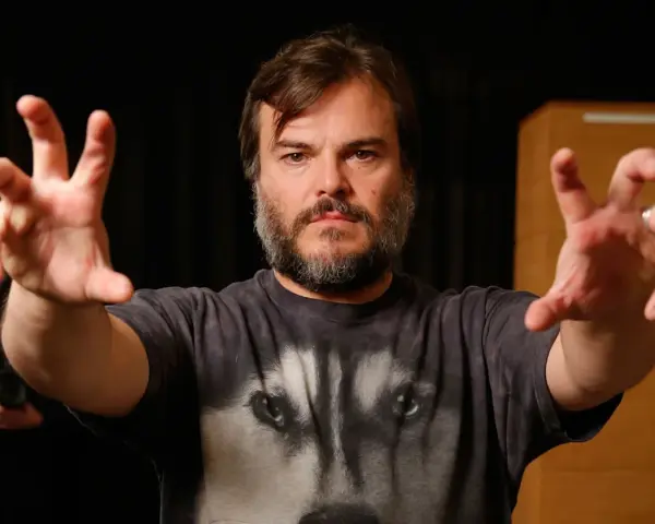 Jack Black w koszulce z wilkiem, z wyciągniętymi rękami. Ciekawe, ile lat ma Jack Black, gdy tak energicznie gestykuluje?