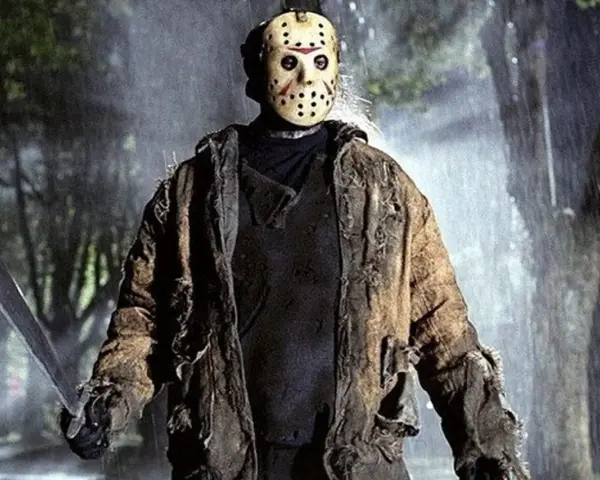 Jason Voorhees, ikona horrorów, w swojej zniszczonej kurtce i z maczetą, stoi w deszczu.