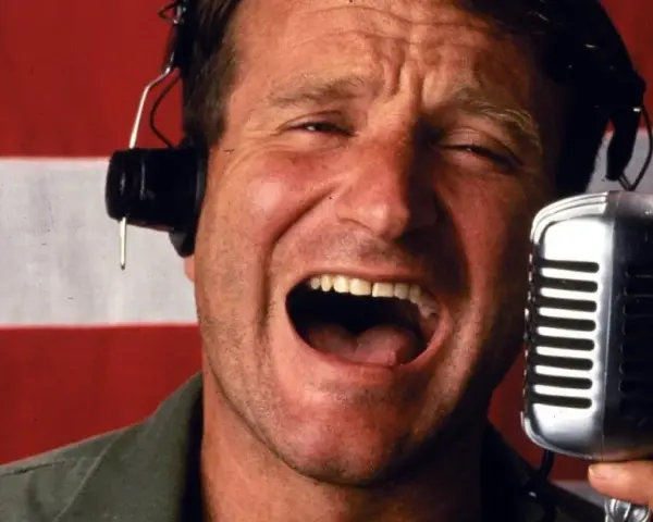 Robin Williams z mikrofonem i słuchawkami na tle flagi. W jakich filmach grał Robin Williams?