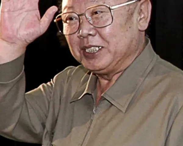 Kim Jong Il w okularach, machający ręką.