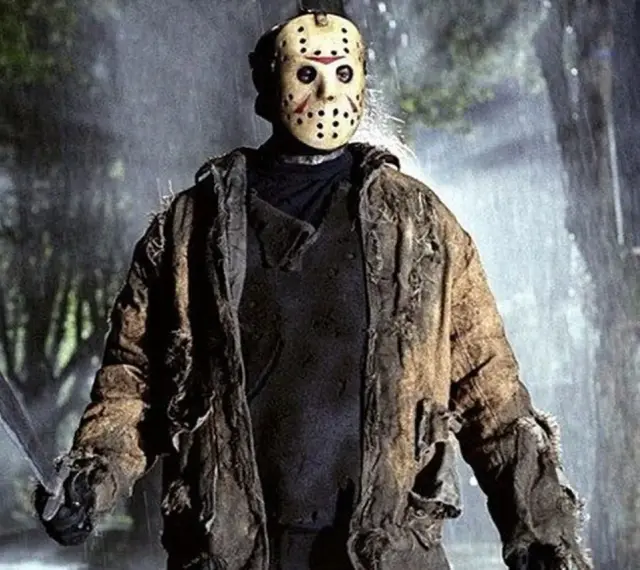 Jason Voorhees, ikona horrorów, w swojej zniszczonej kurtce i z maczetą, stoi w deszczu.