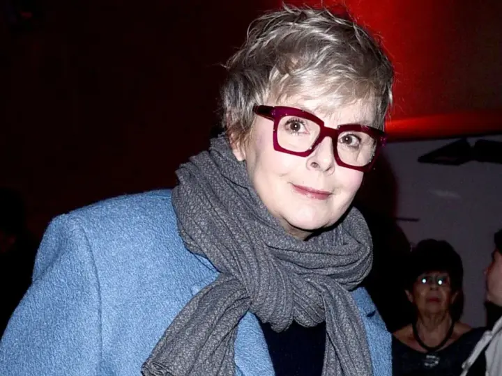 Karolina Korwin Piotrowska w okularach i niebieskim płaszczu, z szarym szalem na szyi.