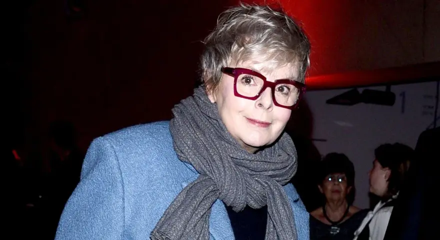 Karolina Korwin Piotrowska w okularach i niebieskim płaszczu, z szarym szalem na szyi.