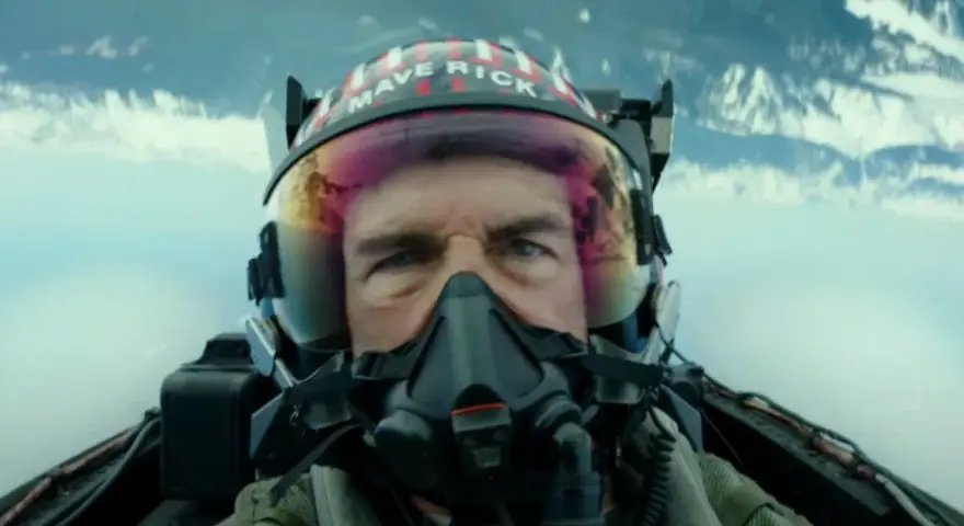 Tom Cruise jako Maverick w hełmie z napisem "MAVERICK" w filmie Top Gun: Maverick. Intensywne spojrzenie pilota w kokpicie myśliwca.