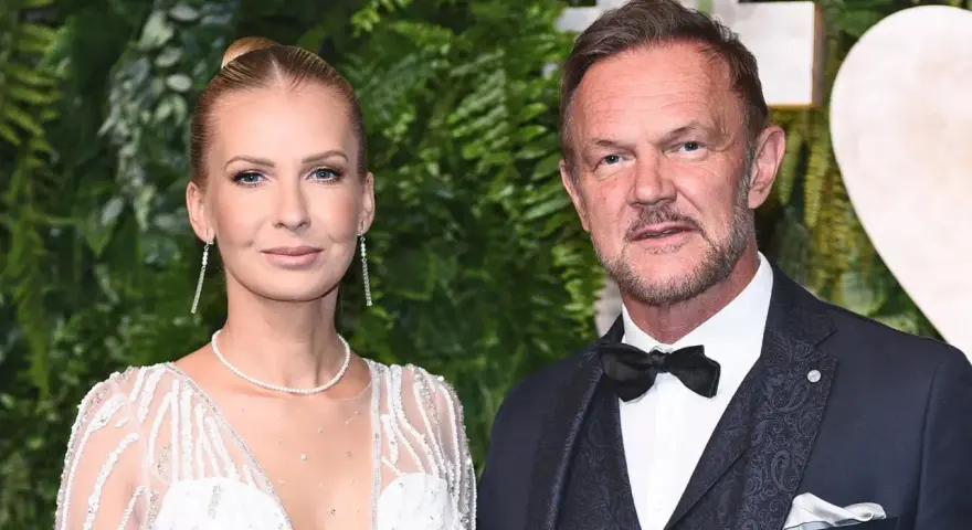 Cezary Pazura z żoną Edytą na ściance. Ona w białej, zdobionej sukni, on w eleganckim garniturze.