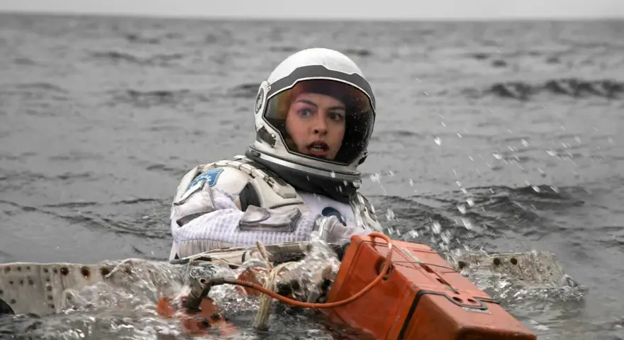 Astronautka w skafandrze z filmu Interstellar 2 w wodzie, z pomarańczowym urządzeniem.