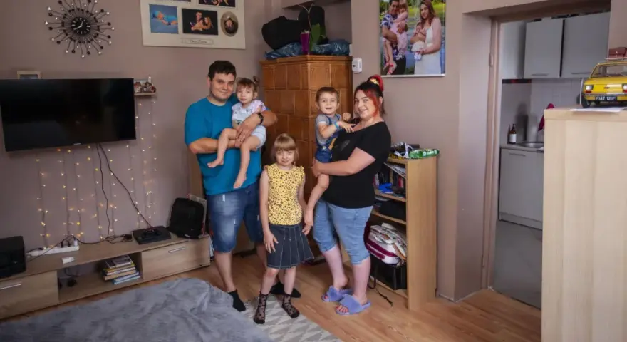 Rodzina z trójką dzieci pozuje do zdjęcia w salonie. W tle widać zdjęcia, telewizor i ozdobne lampki. Ich życie na kredyt nie przeszkadza im w cieszeniu się chwilą.
