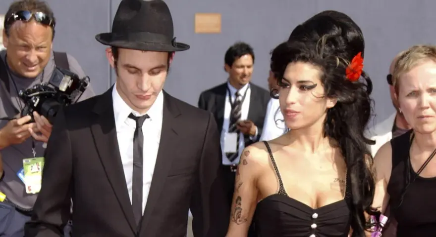 Blake Fielder-Civil w czarnym garniturze i kapeluszu obok Amy Winehouse z czerwoną różą we włosach.