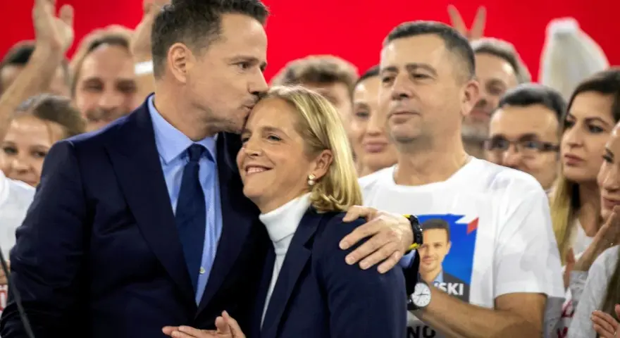 Rafał Trzaskowski, choć nie znamy jego dokładnego wieku, czule całuje żonę na tle tłumu.