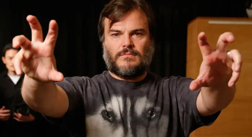 Jack Black w koszulce z wilkiem, z wyciągniętymi rękami. Ciekawe, ile lat ma Jack Black, gdy tak energicznie gestykuluje?