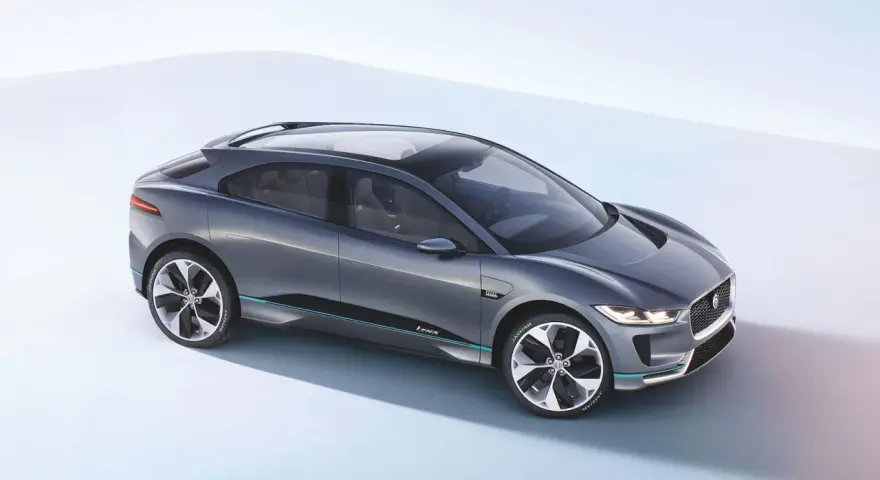 Elegancki, szary Jaguar I-PACE, niczym czarny jaguar gotowy do skoku, prezentuje swoją aerodynamiczną sylwetkę na jasnym tle.
