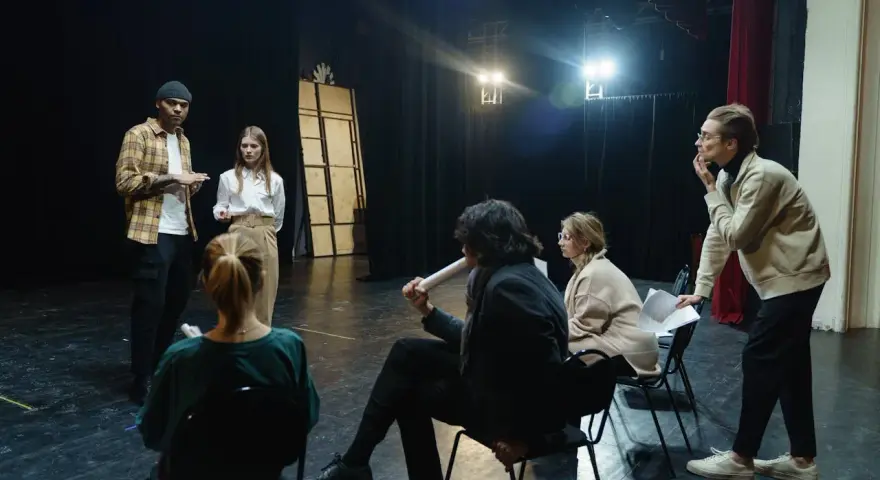 Aktorzy na próbie dyskutują o scenariuszu. Zastanawiają się, ile zarabia reżyser, gdy ich własne pensje są niepewne.