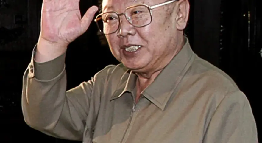 Kim Jong Il w okularach, machający ręką.