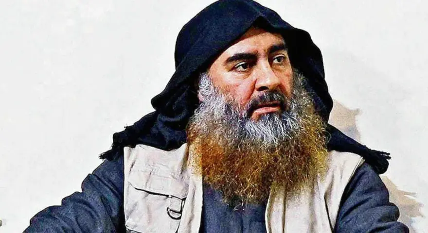 Mężczyzna z długą, siwiejącą brodą i czarnym nakryciem głowy, przypominający Abu Bakra al-Baghdadiego, siedzi w jasnym ubraniu.