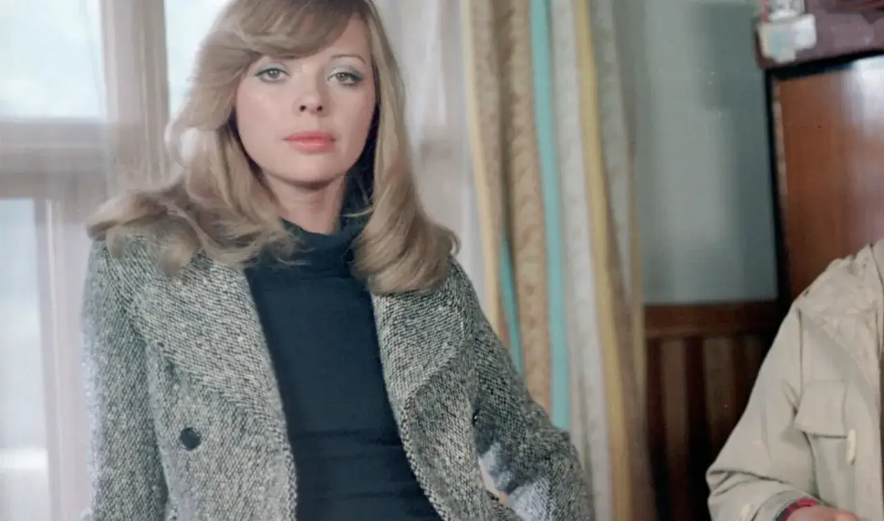 Barbara Kwiatkowska Lass w eleganckim płaszczu, z burzą blond włosów i spojrzeniem pełnym tajemnicy.
