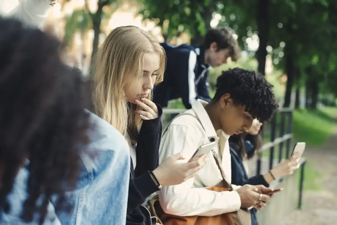 Młodzi ludzie, skupieni na telefonach, czekają na rozpoczęcie roku szkolnego.