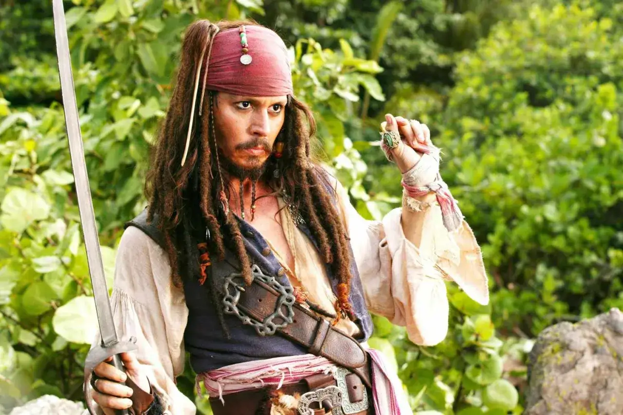Kapitan Jack Sparrow z szablą w dłoni, w pirackim stroju, z charakterystycznymi dredami i czerwoną opaską na głowie.
