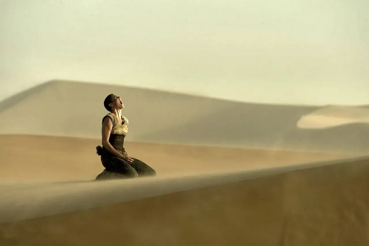Furiosa z filmu Mad Max: Na drodze gniewu klęczy na pustyni, krzycząc w niebo.