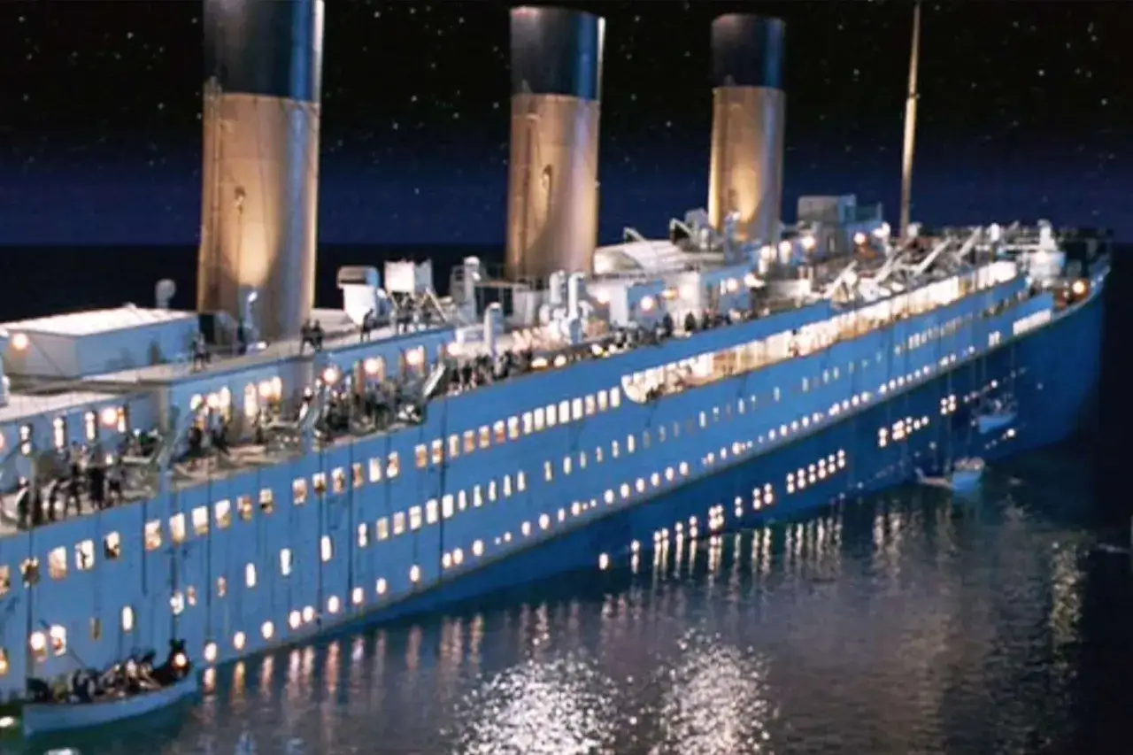 Nocny widok na przechylonego Titanica, z zapalonymi światłami i ludźmi na pokładzie, w mrocznej wodzie.