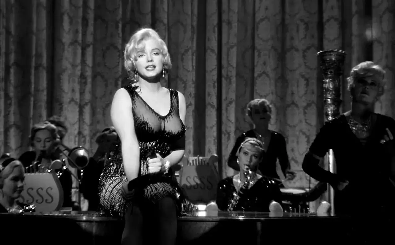 Marilyn Monroe w błyszczącej sukience, pół żartem pół serio, śpiewa dla orkiestry.