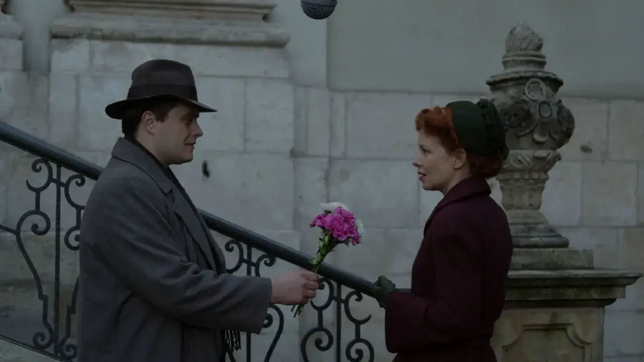 Mężczyzna w kapeluszu wręcza kobiecie bukiet kwiatów. Może to scena z filmu, gdzie szepcze 