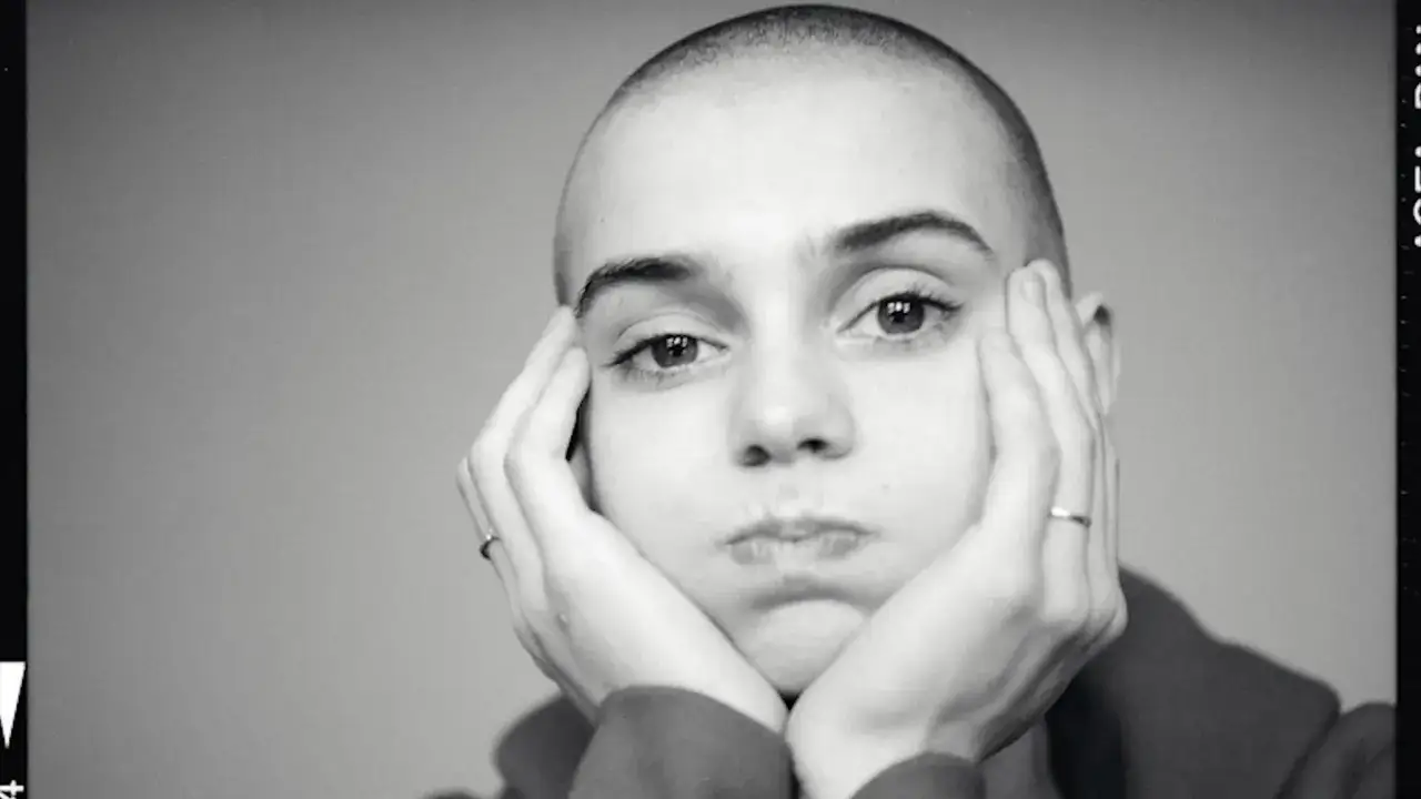 Sinead O'Connor zamyślona, z dłońmi podpartymi pod brodą. Ikoniczny wizerunek artystki.