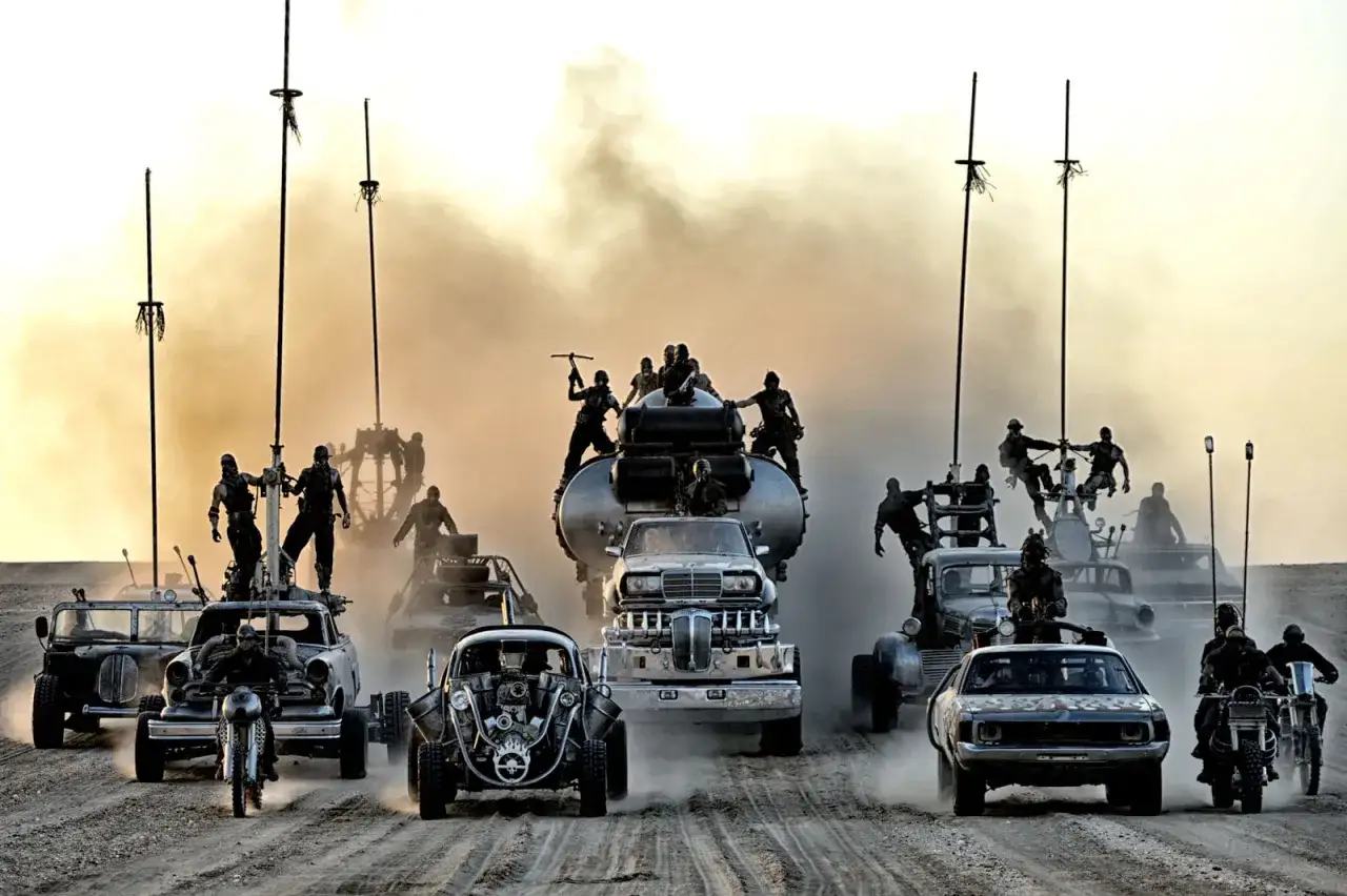Konwój pojazdów w stylu Mad Max na drodze gniewu. Ludzie na pojazdach, kurz i dym tworzą apokaliptyczną atmosferę.