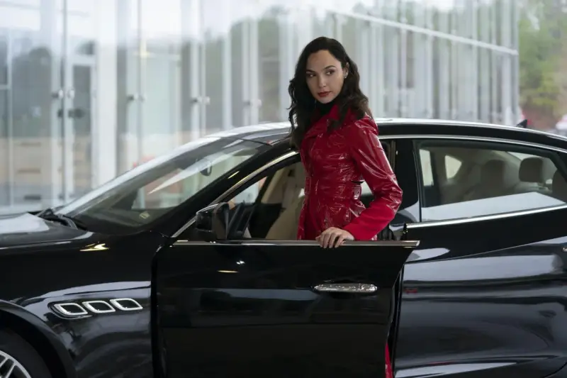 Kobieta w błyszczącym, czerwonym płaszczu opiera się o czarne auto. Wygląda jak z filmu, może to jej czerwona nota 2?