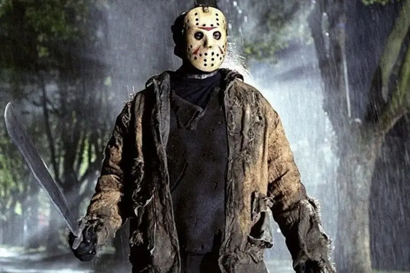 Jason Voorhees, ikona horrorów, w swojej zniszczonej kurtce i z maczetą, stoi w deszczu.